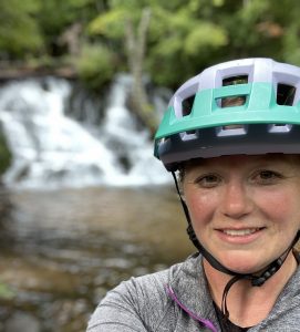 Ski Cats Coordinator Allison Carmody wearing a bicycle helmet in front of a waterfall